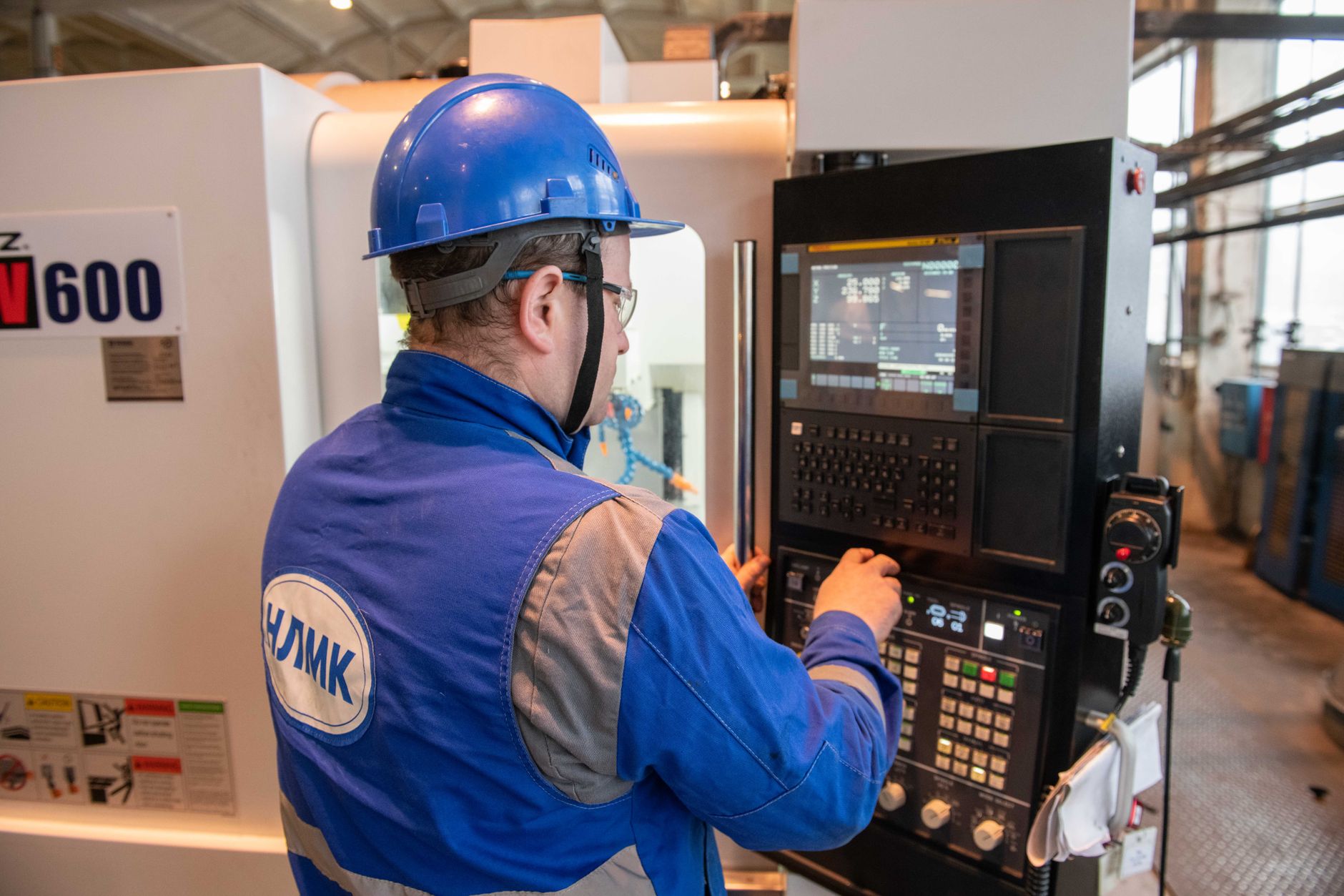 A CNC machinist programming a milling machine control panel on the shop floor