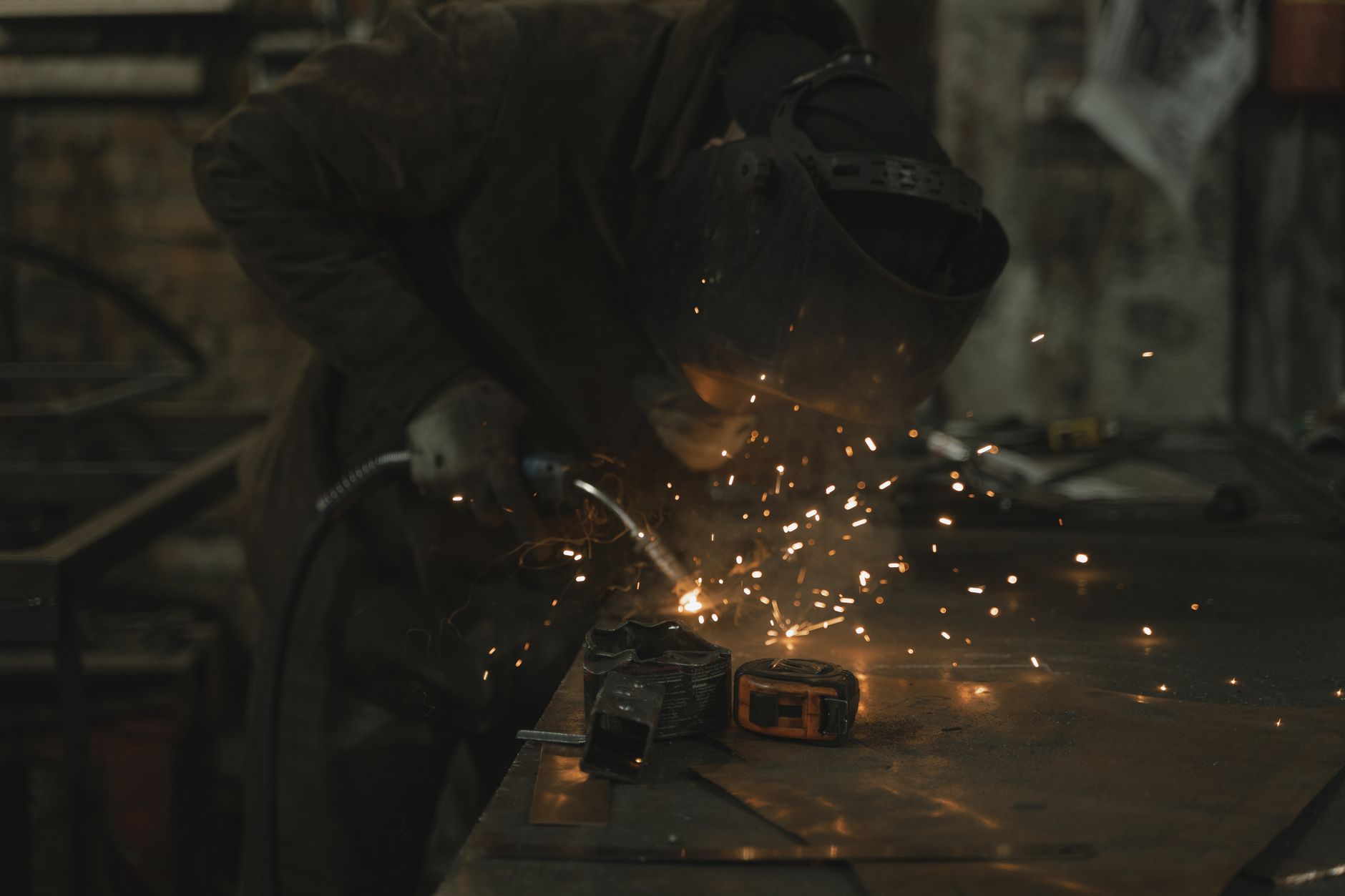 A welder in full safety gear welding a structural steel joint, sparks flying
